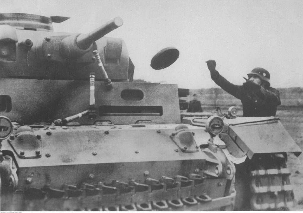 A Volkssturm volunteer throws dummy M24 Stielhandgranades and anti-tank mine at a Panzer III tank during training.