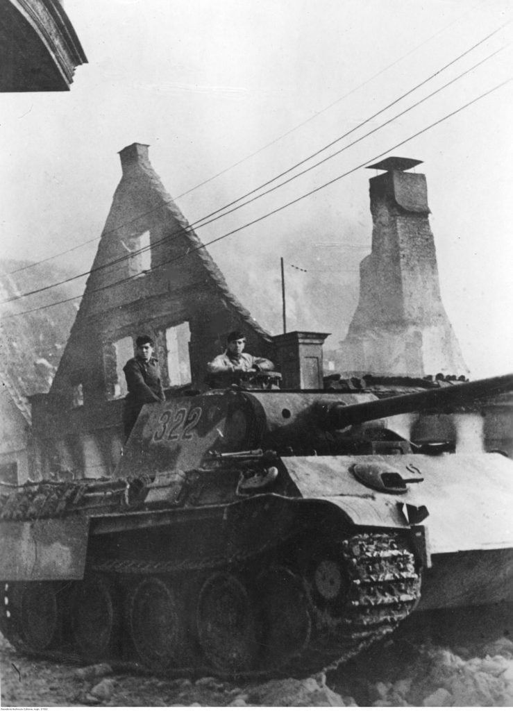 A German PzKpfw V Panther tank drives past a burning house. Date November, 1944, location unknown.