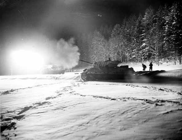 M10 Wolverine American tank destroyers serve as artillery at night in the Sparsbach area, France. They fire two kinds of ammunition: one with a bright powder flash and another with a faint red glow, both targeting enemy positions.